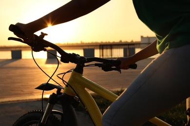 Young woman with bicycle on city waterfront at sunset, closeup