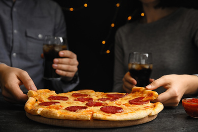 Friends taking tasty pepperoni pizza at table, closeup