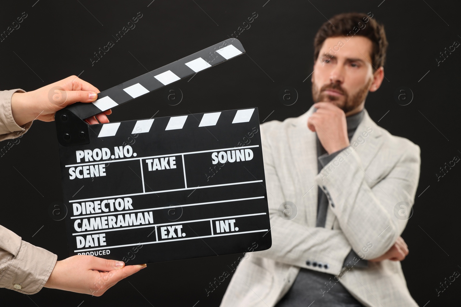 Photo of Actor performing while second assistant camera holding clapperboard on black background, closeup