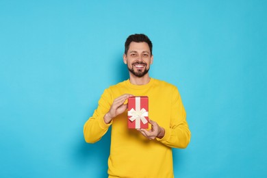 Happy man with gift box on light blue background