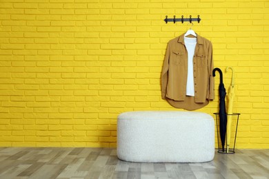Stylish comfortable pouf near yellow brick wall in hallway, space for text