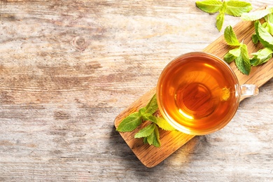Photo of Glass with hot aromatic mint tea and fresh leaves on wooden board, top view