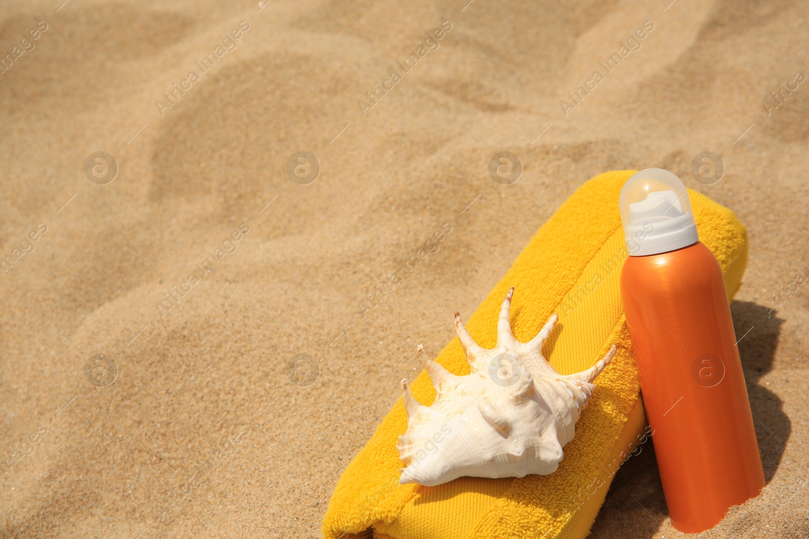 Photo of Sunscreen, seashell and rolled towel on sandy beach, space for text. Sun protection