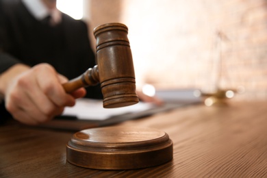 Photo of Judge with gavel at table in courtroom, closeup. Law and justice concept