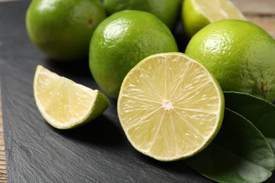 Photo of Fresh limes and green leaves on black board, closeup