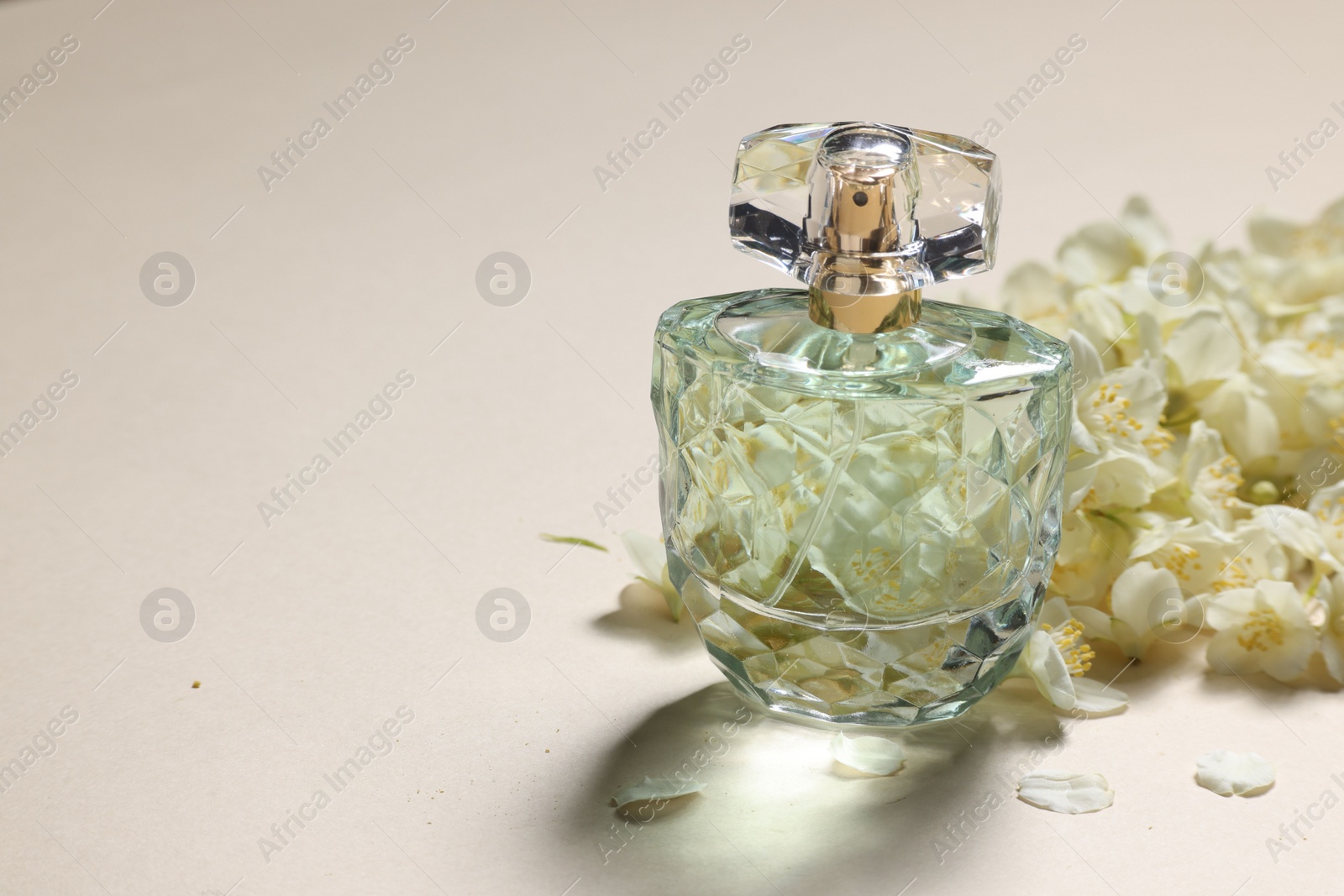 Photo of Bottle of aromatic perfume and jasmine flowers on beige background, closeup. Space for text