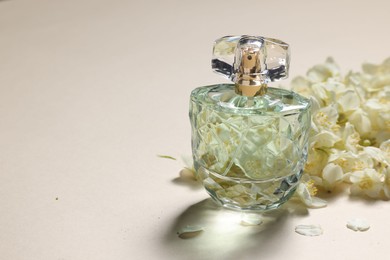 Bottle of aromatic perfume and jasmine flowers on beige background, closeup. Space for text