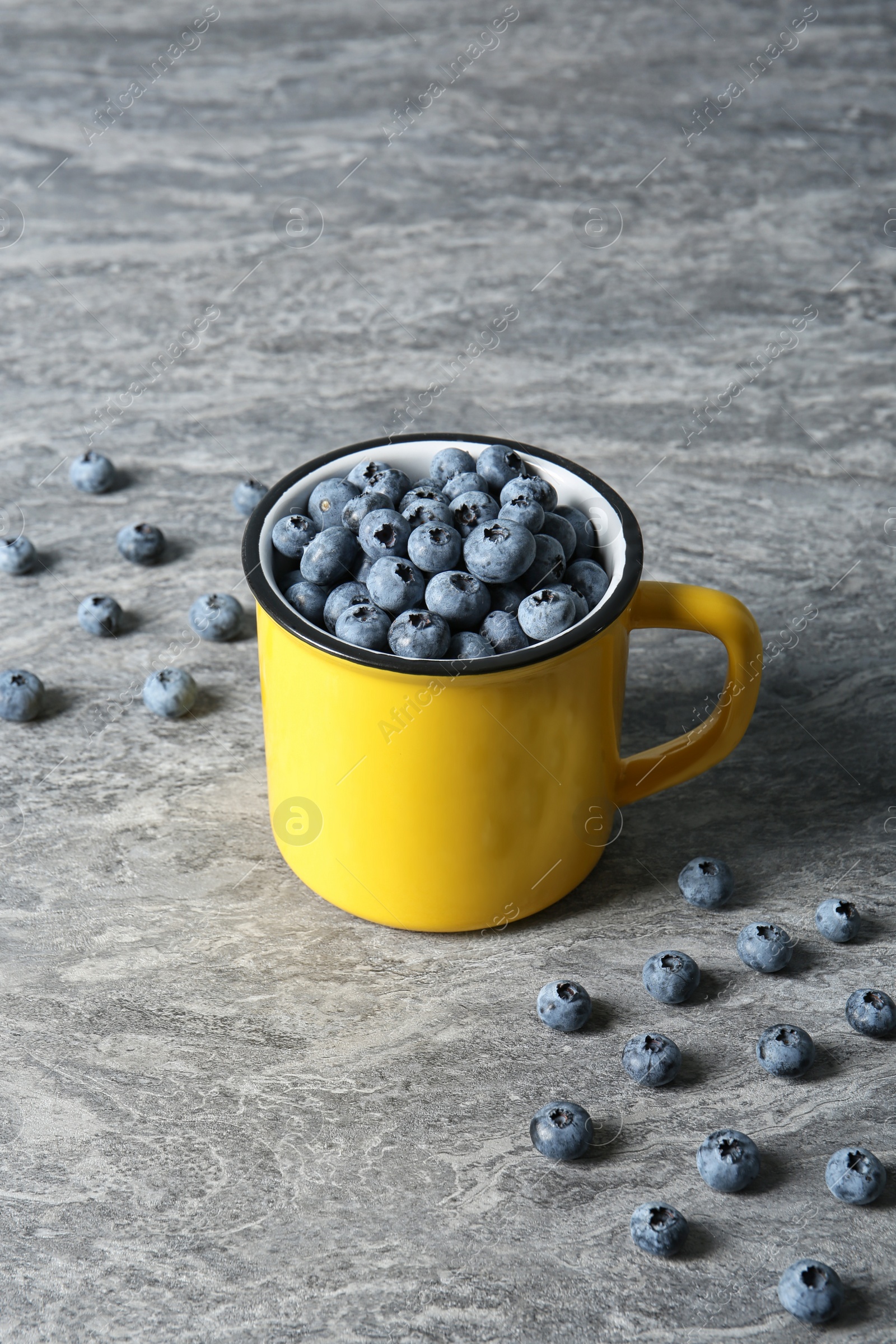 Photo of Fresh blueberries in yellow cup on color table