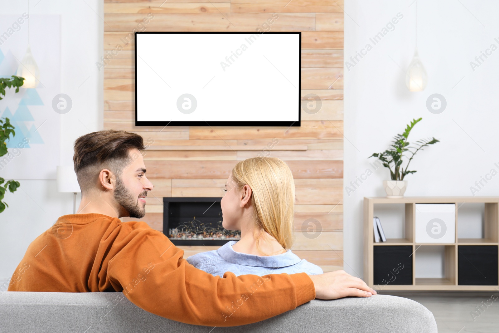 Photo of Couple watching TV on sofa in living room with decorative fireplace