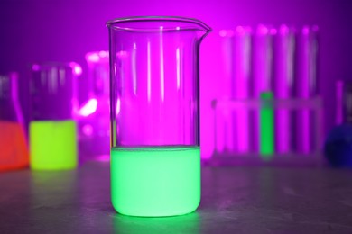 Laboratory beaker with luminous liquid on table against blurred background, closeup