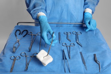 Doctor holding medical forceps with pad near table of different surgical instruments on light background, closeup