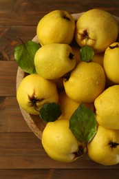 Photo of Tasty ripe quince fruits with water drops in bowl on wooden table, top view