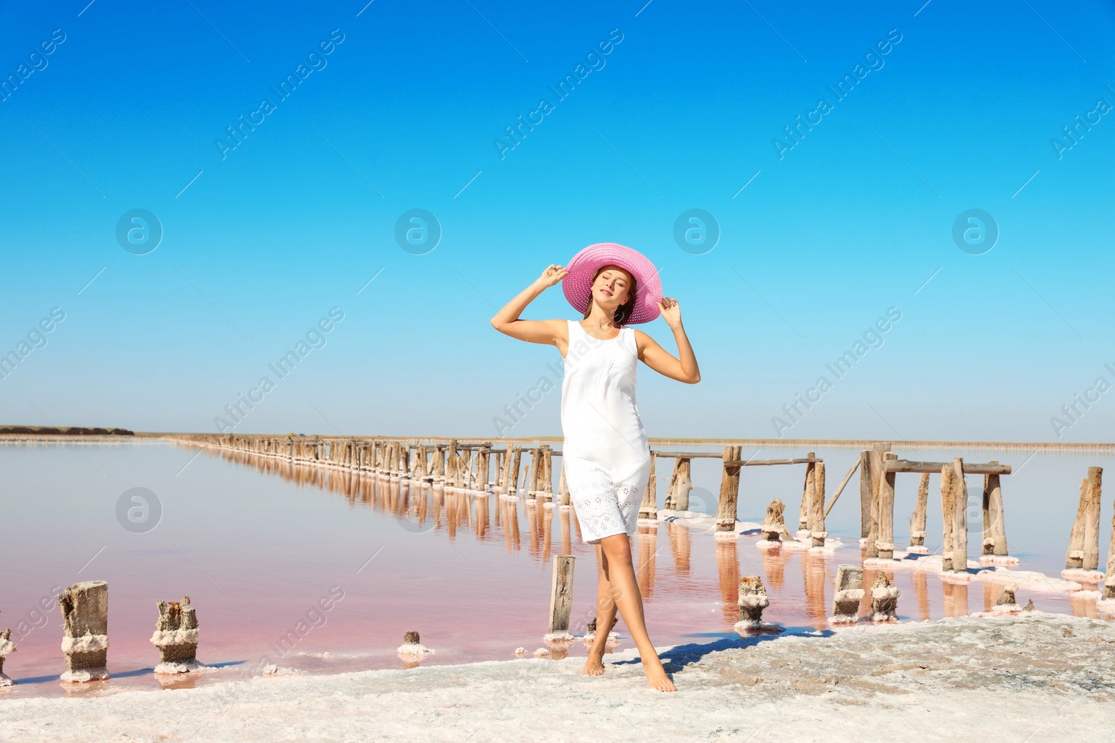 Photo of Beautiful woman with hat posing near pink lake on summer day