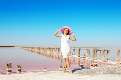 Beautiful woman with hat posing near pink lake on summer day