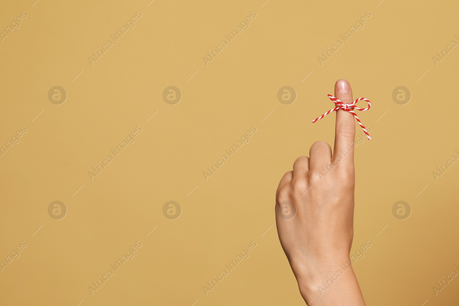 Photo of Woman showing index finger with tied bow as reminder on light brown background, closeup. Space for text