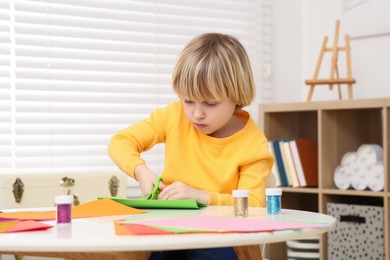 Photo of Cute little boy cutting green paper at desk in room. Home workplace