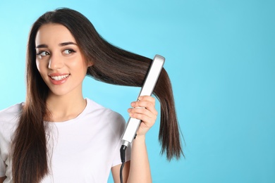 Happy woman using hair iron on color background. Space for text