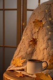 Cup of aromatic tea, sweater and autumn leaves on wooden chair indoors, space for text