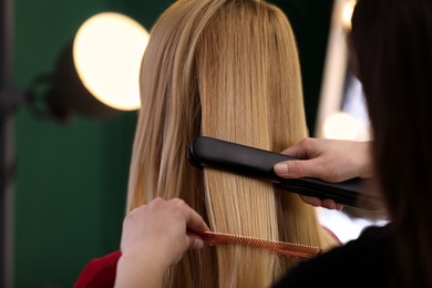 Stylist straightening woman's hair with flat iron in salon