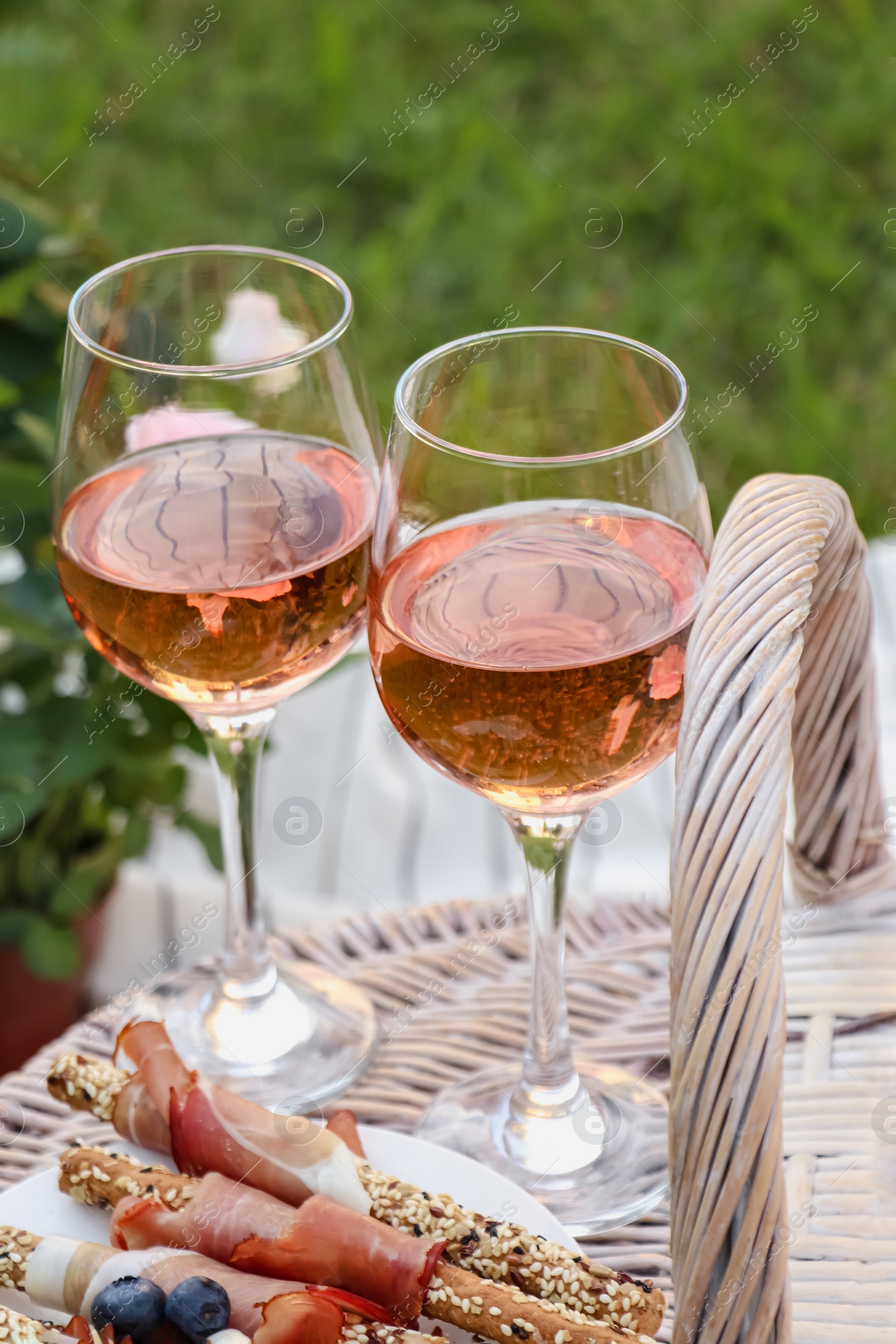 Photo of Glasses of delicious rose wine and food on picnic basket outdoors