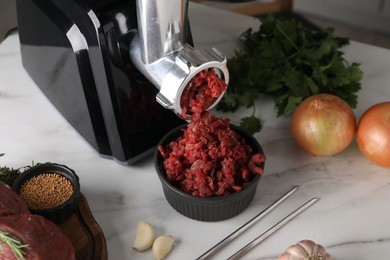 Photo of Electric meat grinder with beef mince and products on white marble table in kitchen