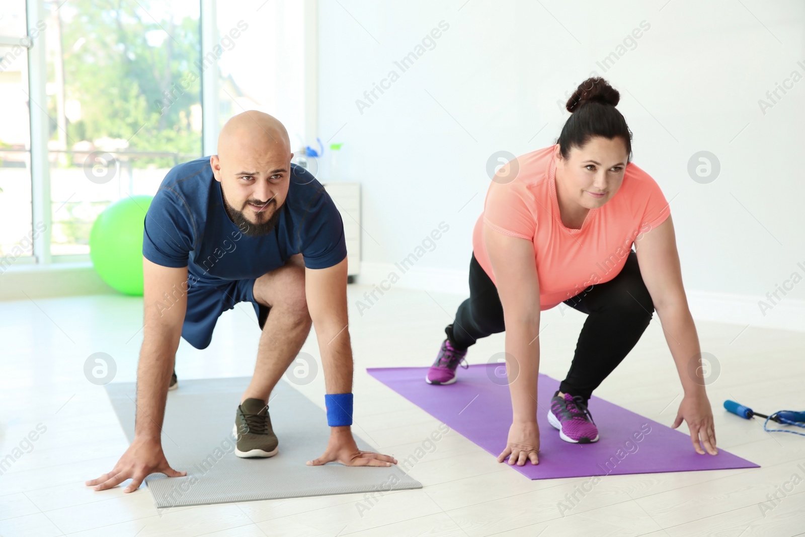 Photo of Overweight man and woman doing exercise on mats in gym