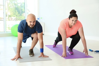 Photo of Overweight man and woman doing exercise on mats in gym