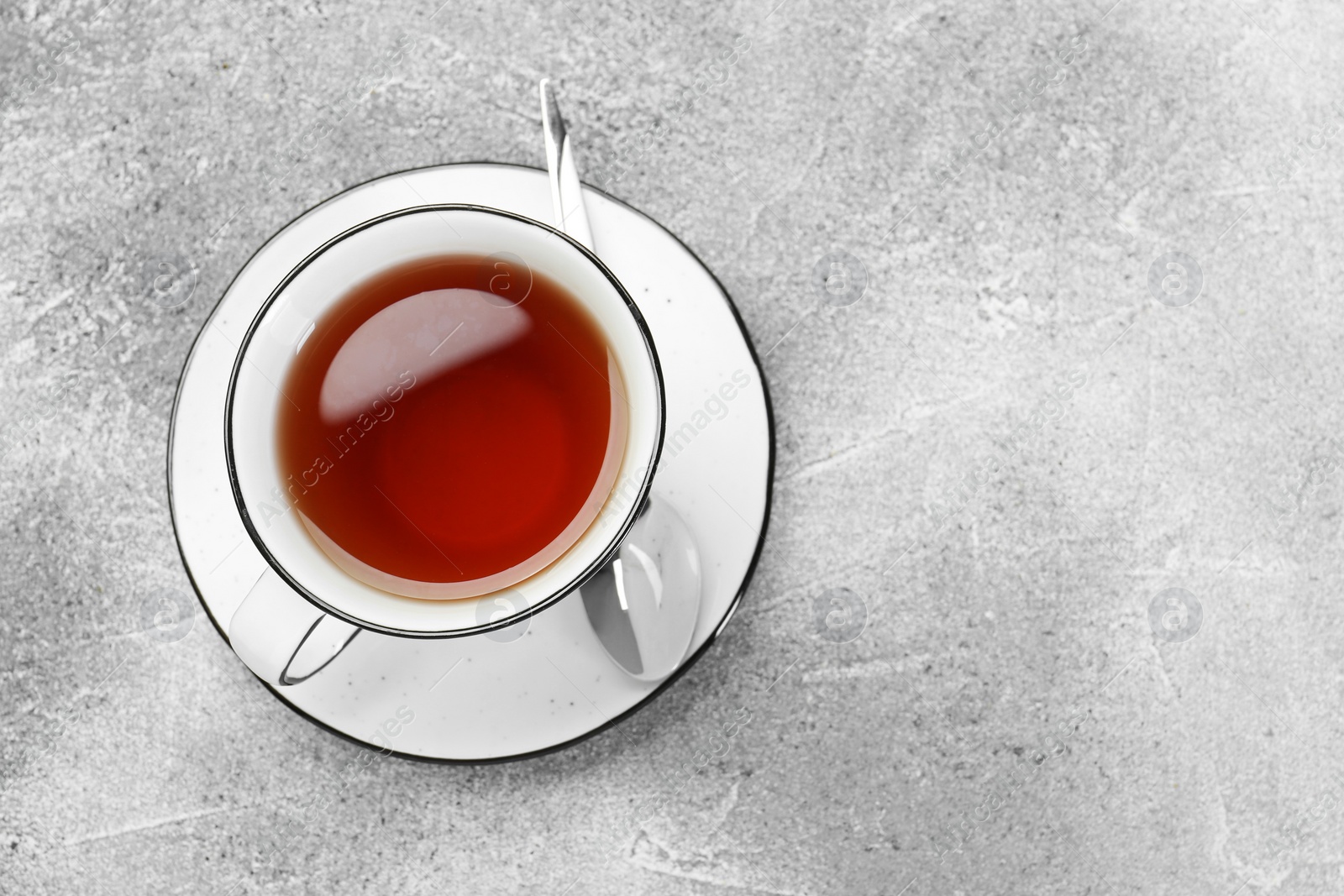 Photo of Aromatic tea in cup and spoon on grey table, top view. Space for text