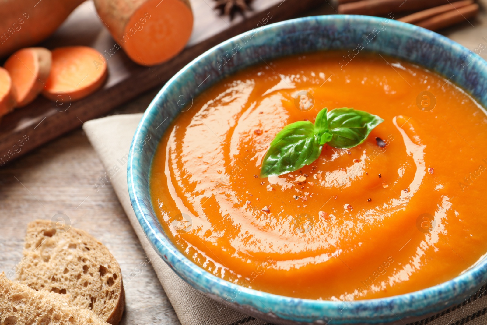 Photo of Bowl of tasty sweet potato soup served on table, closeup. Space for text