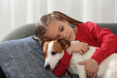 Photo of Cute girl hugging her dog on sofa indoors. Adorable pet