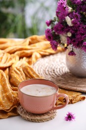 Cup of aromatic coffee, beautiful flowers and orange cloth on white table