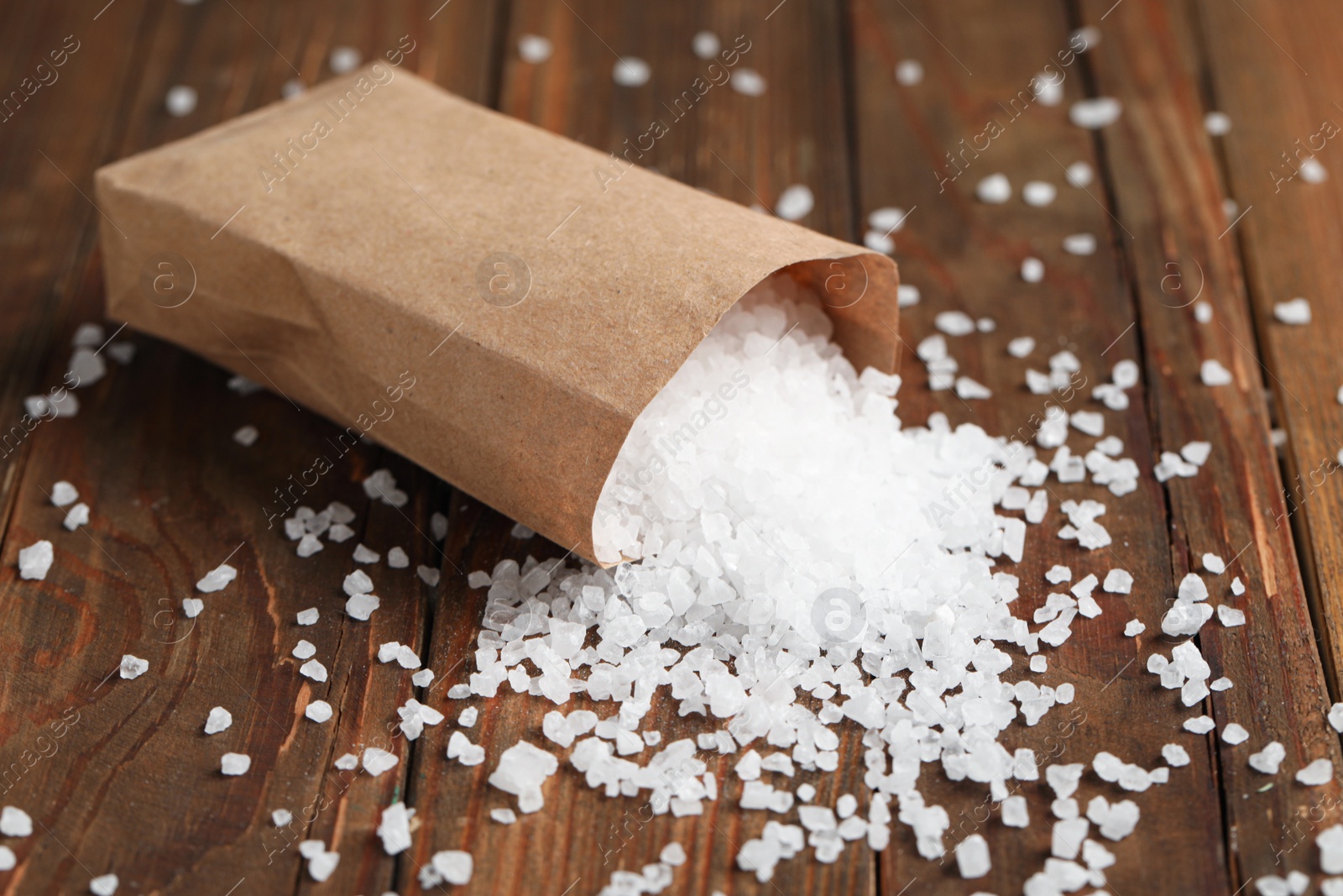 Photo of Overturned paper bag with natural sea salt on wooden table