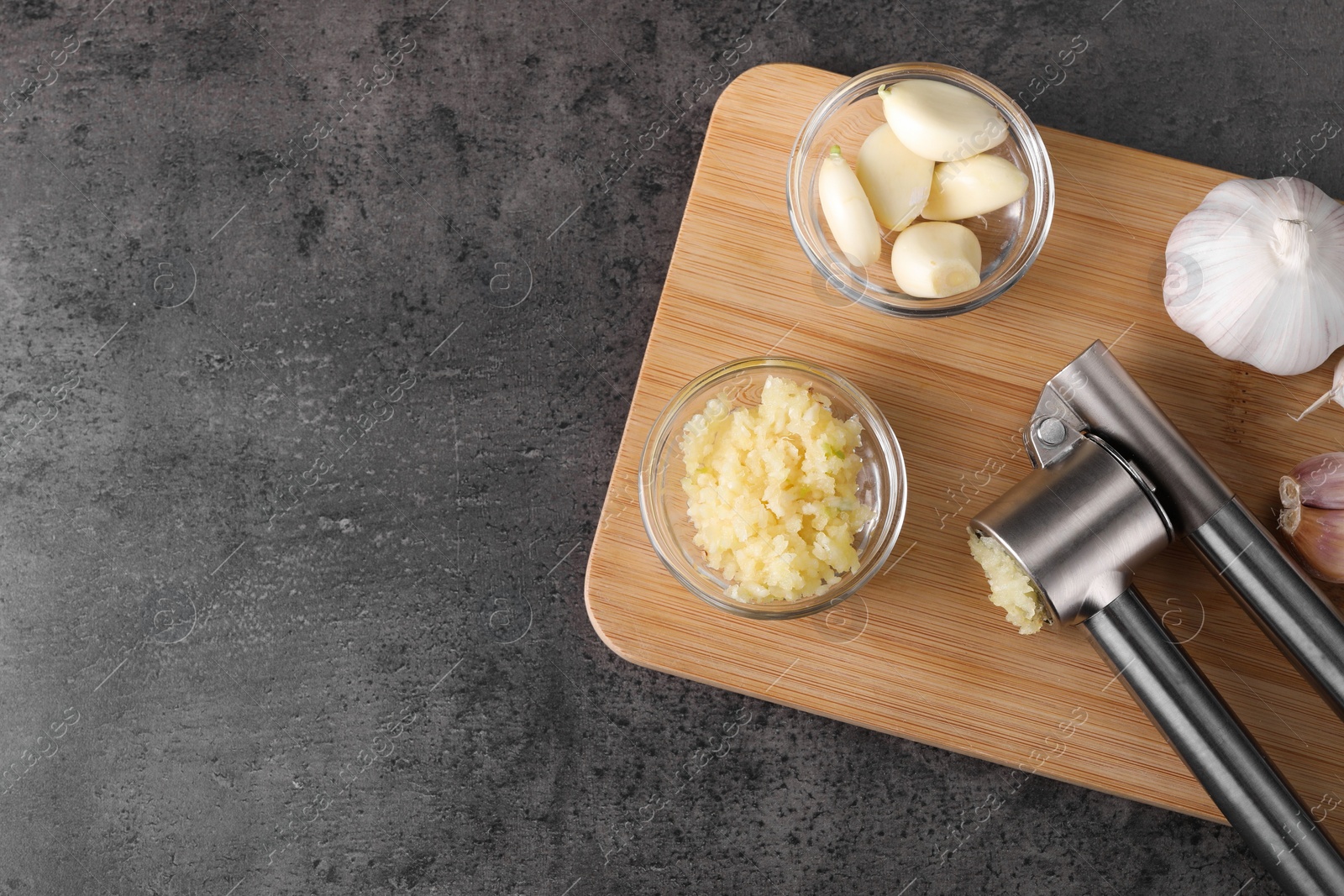 Photo of Garlic press, cloves and mince on wooden table, top view. Space for text