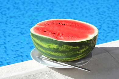 Photo of Half of fresh juicy watermelon on white plate near swimming pool outdoors