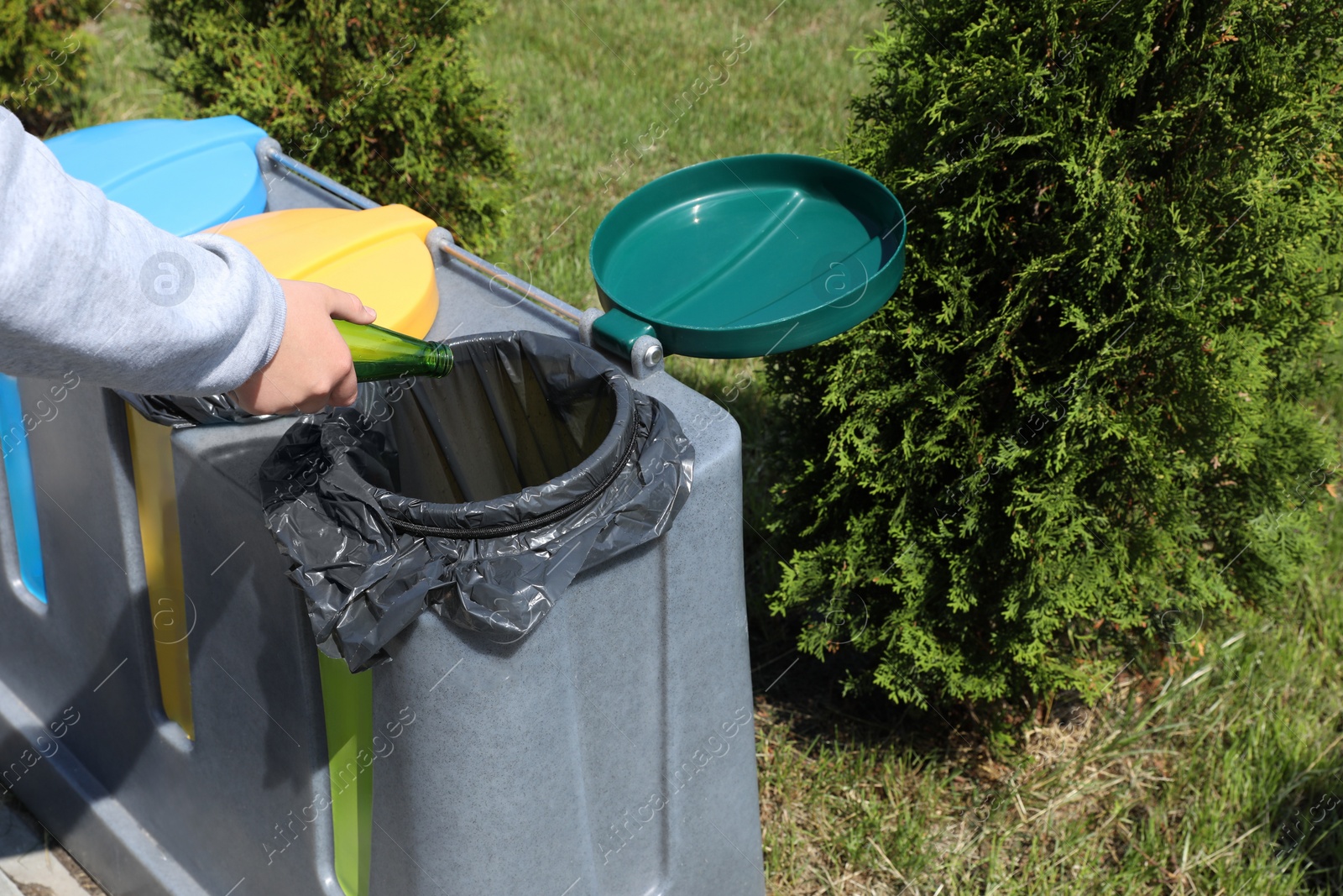 Photo of Woman throwing glass bottle in bin outdoors, closeup. Recycling concept