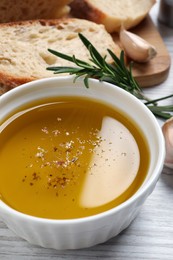 Bowl of fresh oil, bread, rosemary and garlic on white wooden table, closeup