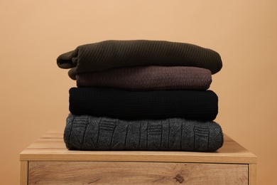 Photo of Stack of casual sweaters on wooden table against light brown background