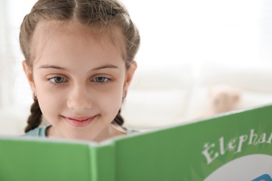 Photo of Cute little girl reading book at home, closeup