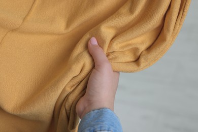 Photo of Woman touching clothes made of soft yellow fabric indoors, closeup