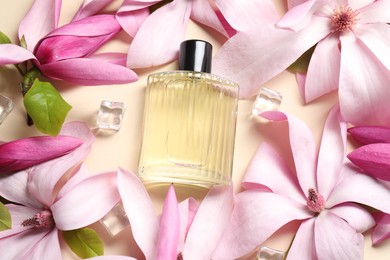 Beautiful pink magnolia flowers, bottle of perfume and ice cubes on beige background, flat lay