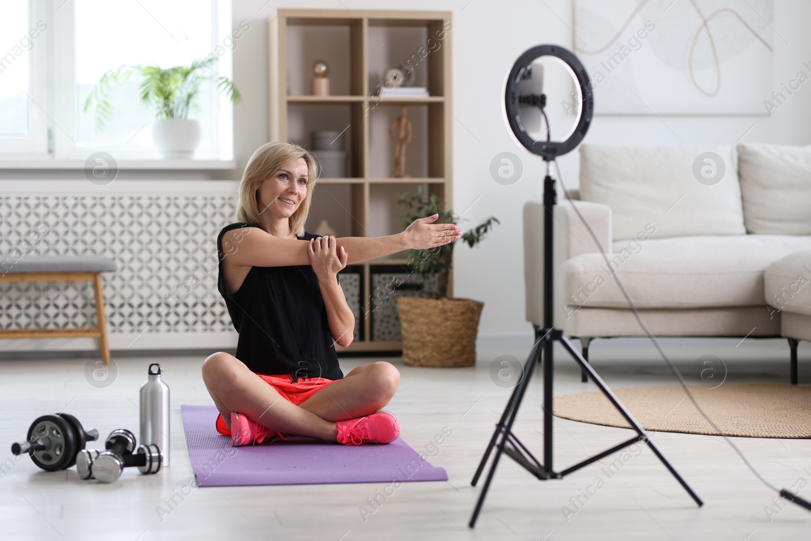 Photo of Smiling sports blogger streaming online fitness lesson with smartphone at home