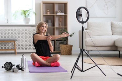 Photo of Smiling sports blogger streaming online fitness lesson with smartphone at home