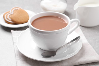 Photo of Delicious tea with milk in white cup near cookies on grey table