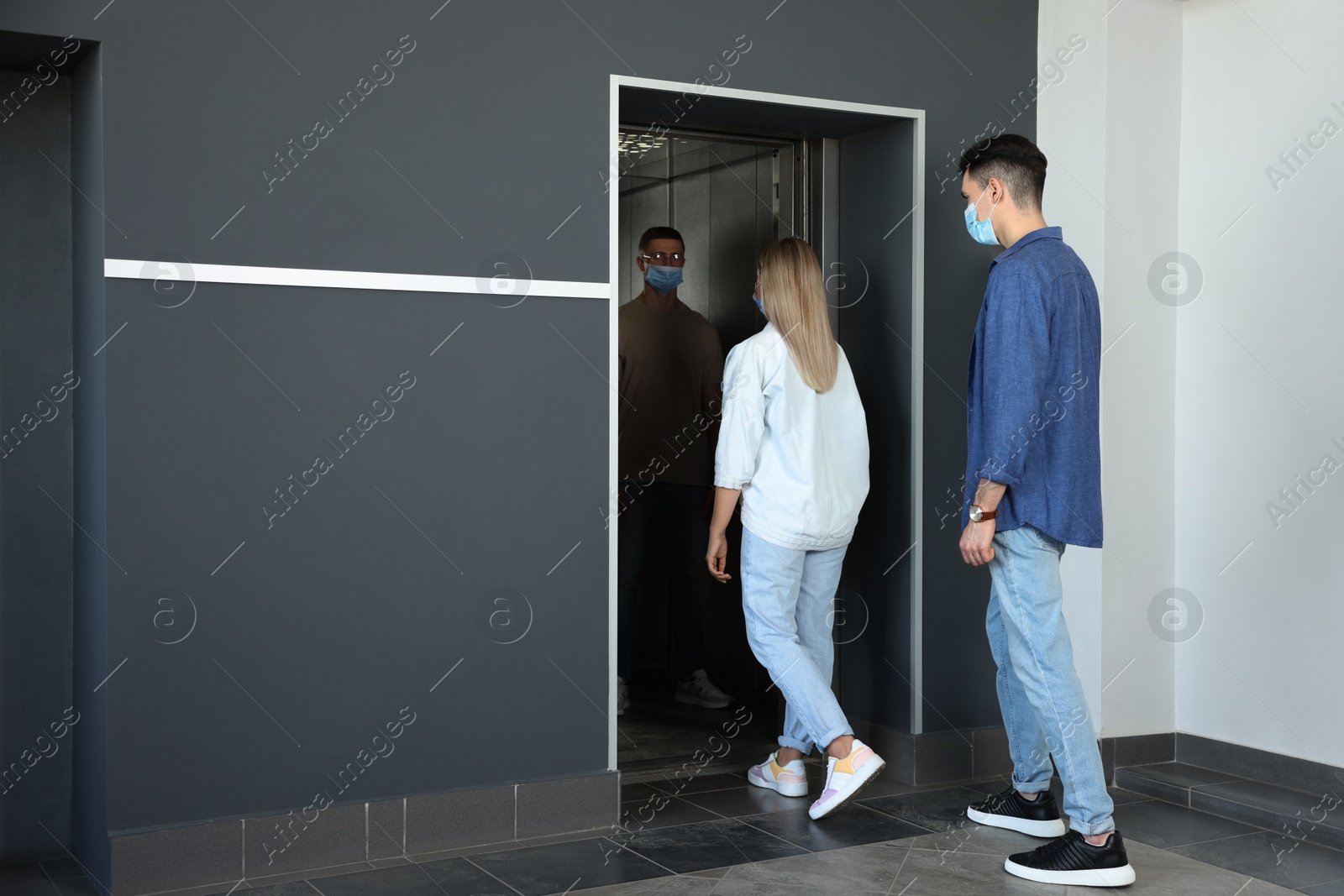 Photo of Group of people in face masks entering elevator, back view. Protective measure