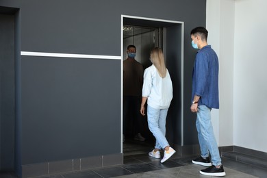 Photo of Group of people in face masks entering elevator, back view. Protective measure