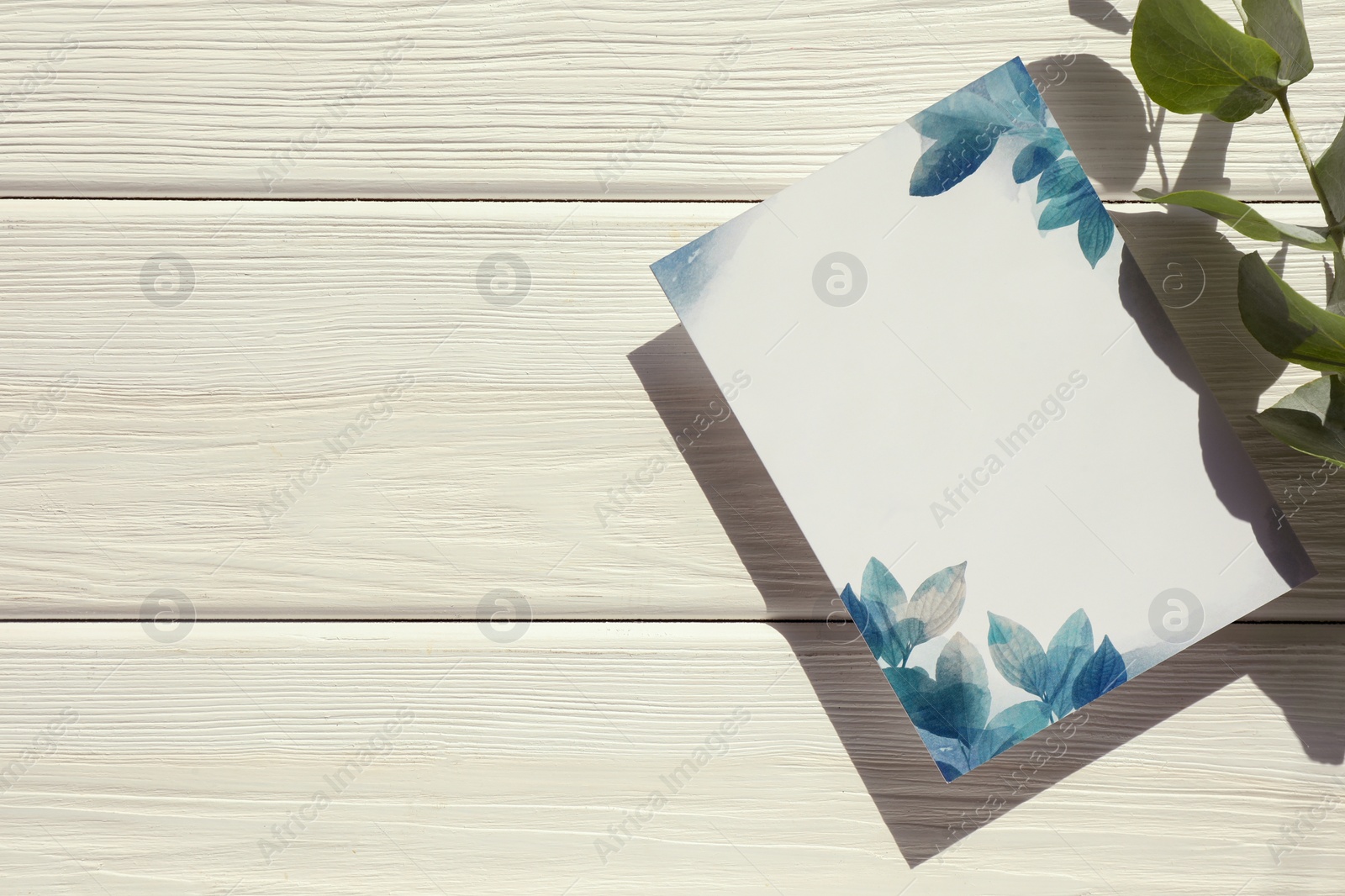 Photo of Beautiful card with word Invitation and green leaves on white wooden table, top view. Space for text