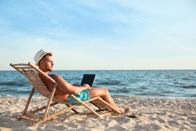 Photo of Young man with laptop in deck chair on beach