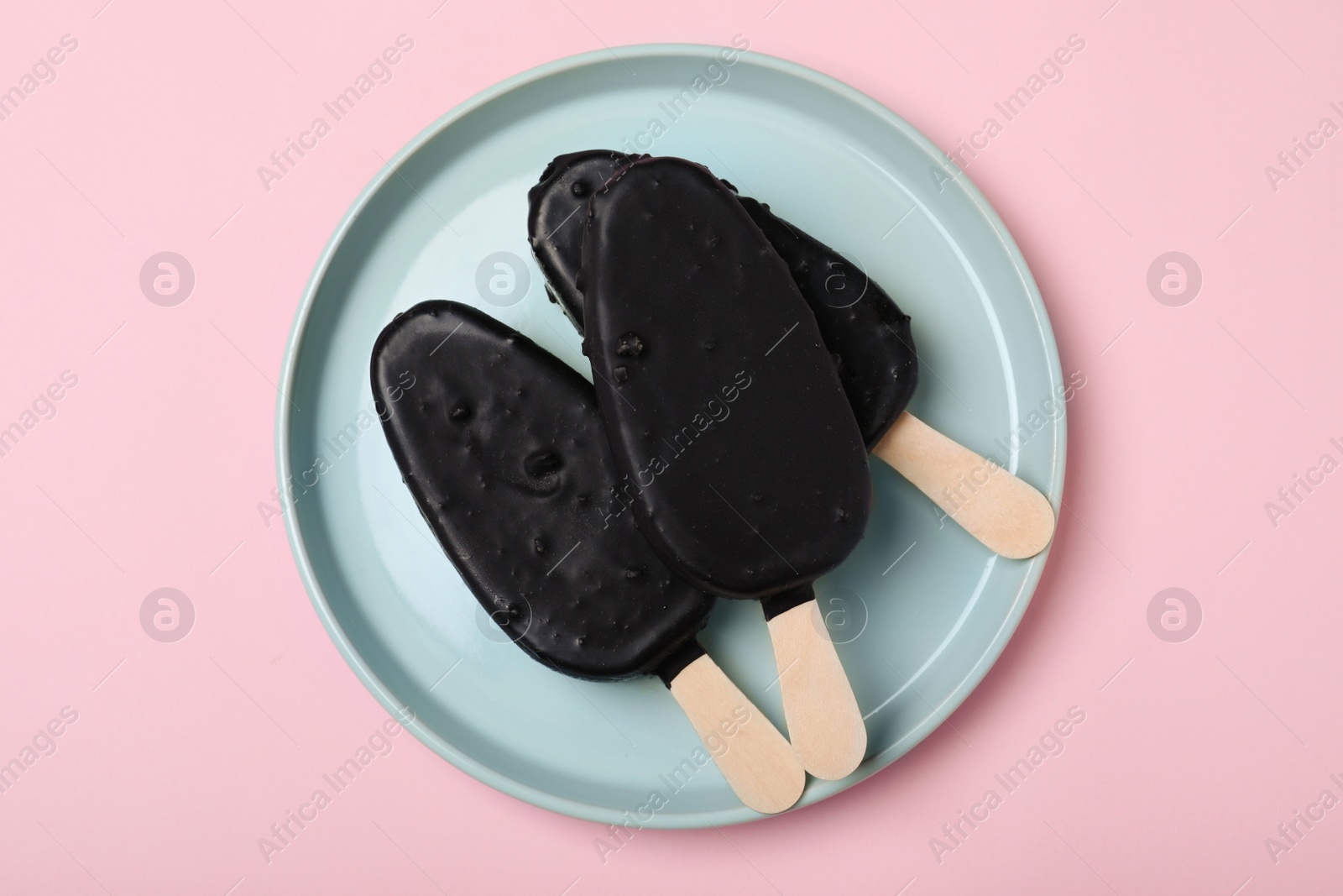 Photo of Plate with glazed ice cream bars on pink background, top view