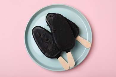 Plate with glazed ice cream bars on pink background, top view