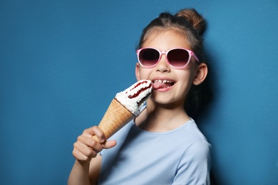 Adorable little girl with delicious ice cream against color background